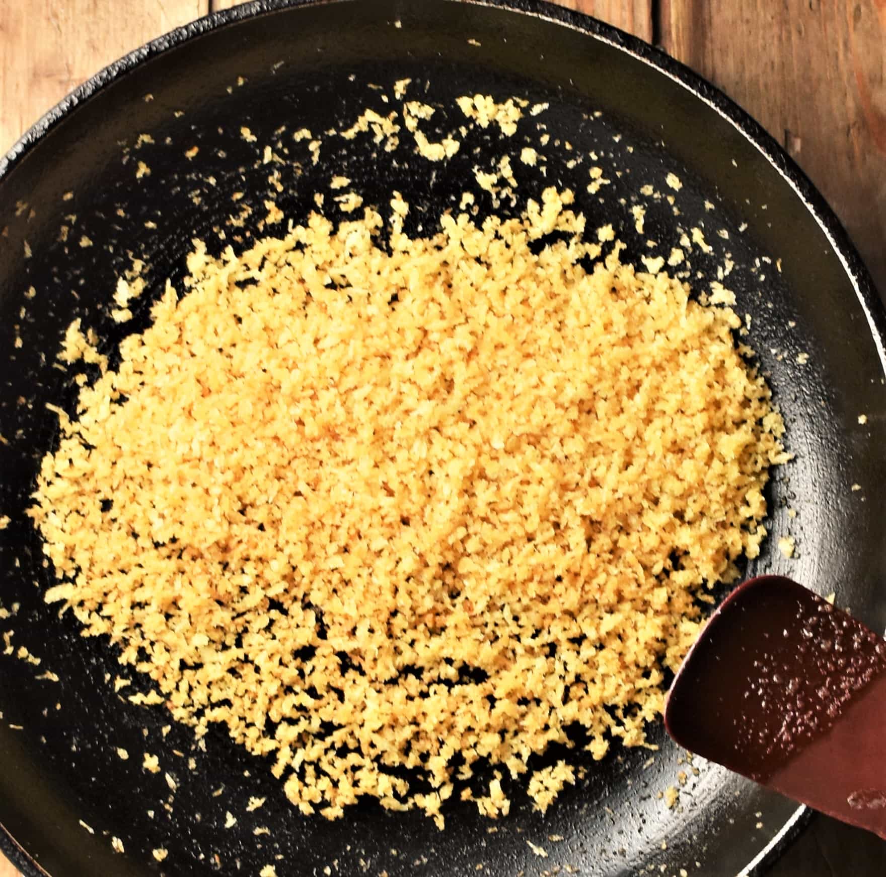 Top down view of toasted panko breadcrumbs in skillet with spatula in bottom right corner.