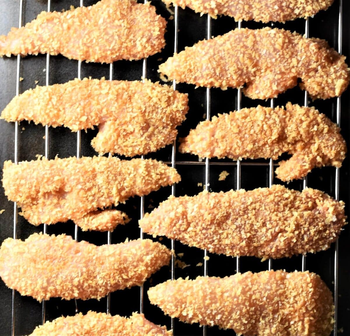 Unbaked bread chicken tenders on top of rack.