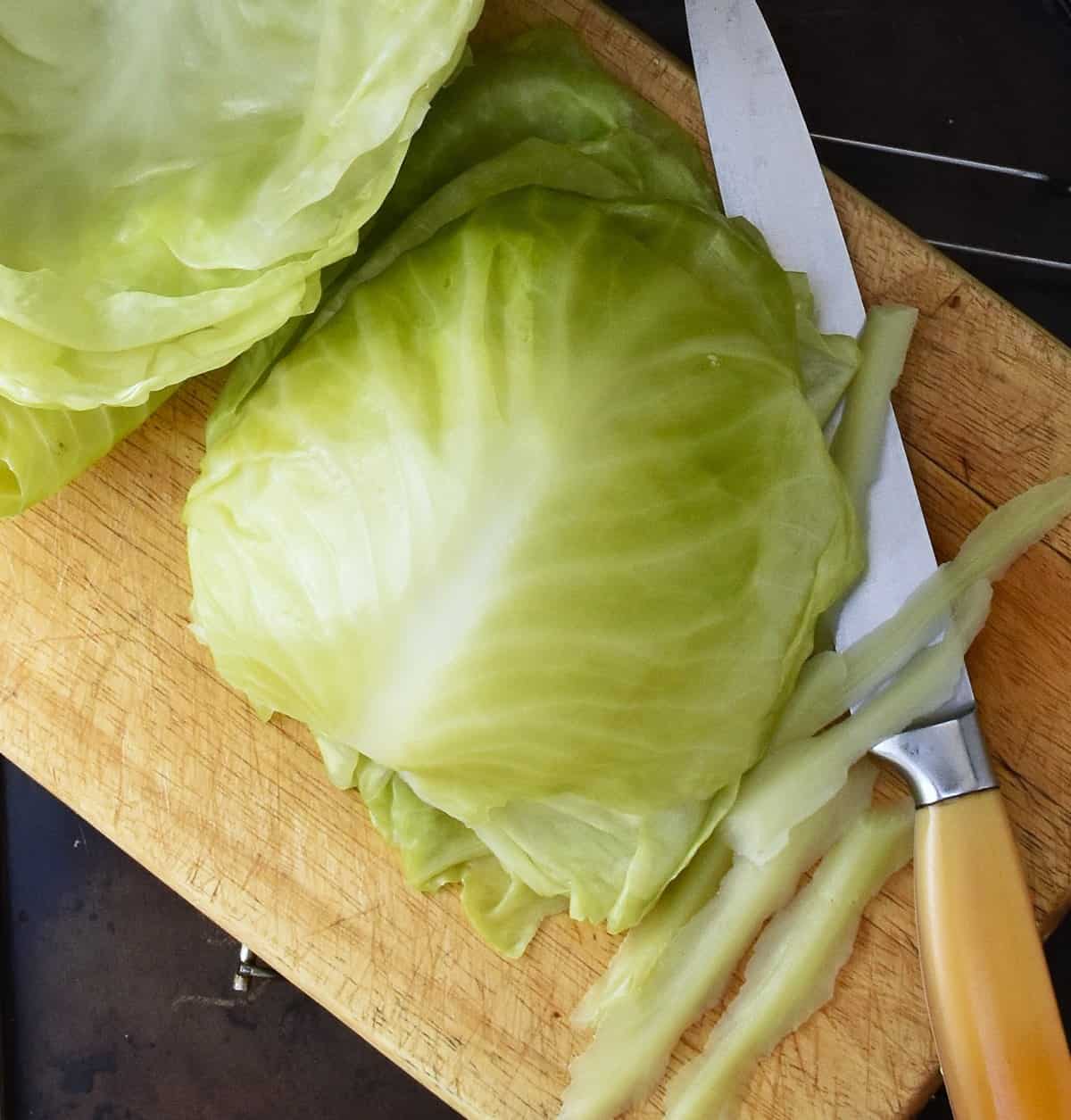 Cabbage leaves piled on wooden board with knife.