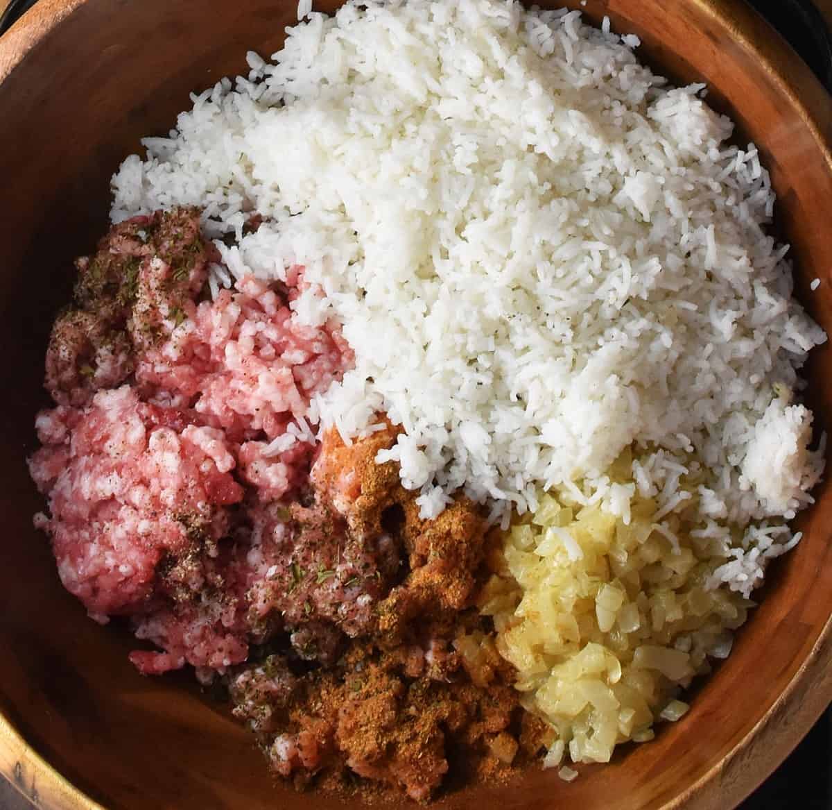 Cooked rice, ground pork, chopped onion and herbs in wooden bowl.