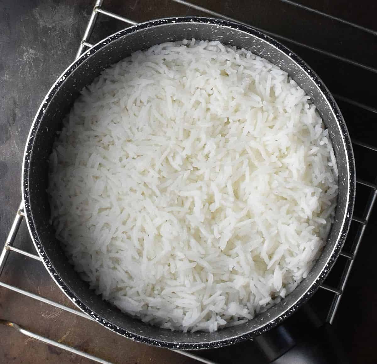 Cooked rice in black pot on top of cooling rack.