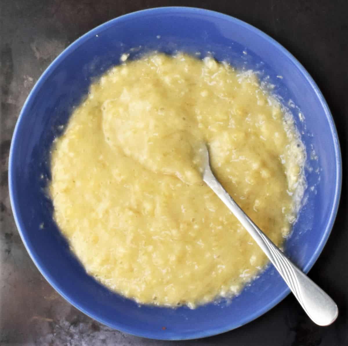 Mashed banana with fork in blue bowl.