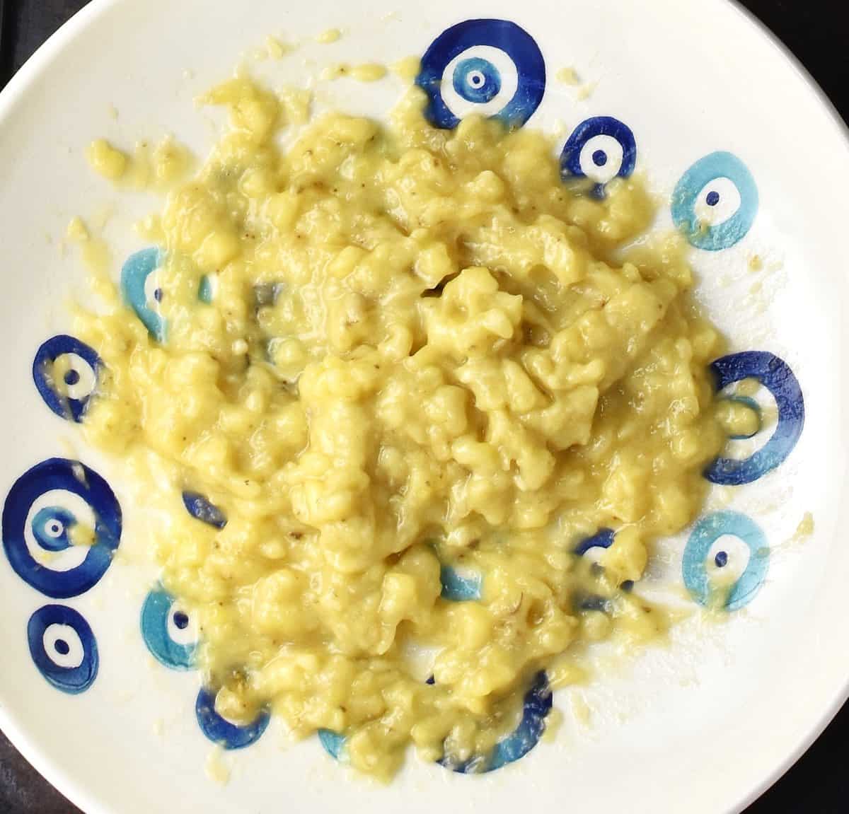 Top down view of mashed banana in large shallow bowl with blue design.
