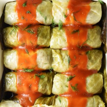 Top down view of Polish cabbage rolls in single layer topped with tomato sauce.
