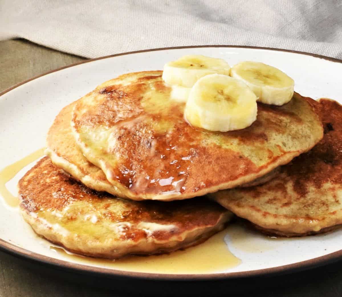 Side view of pancakes with slices of banana and maple syrup.