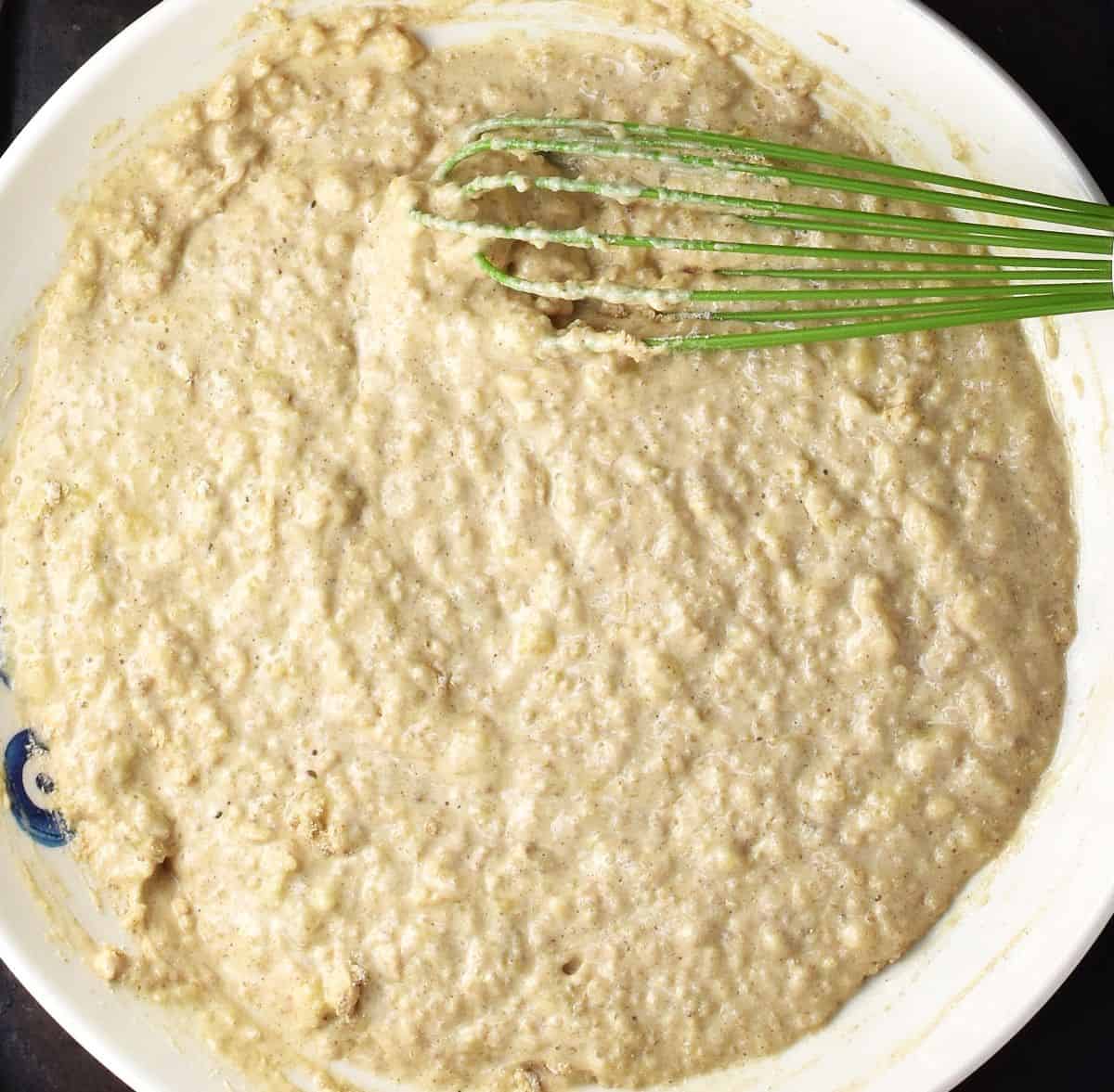 Quinoa banana pancake batter in white, shallow bowl with green whisk.