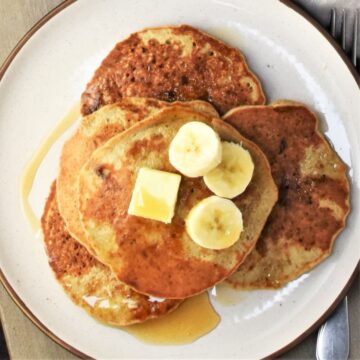 Top down view of quinoa pancakes with banana slices and maple syrup.