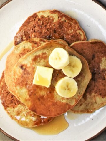 Top down view of quinoa pancakes with banana slices and maple syrup.