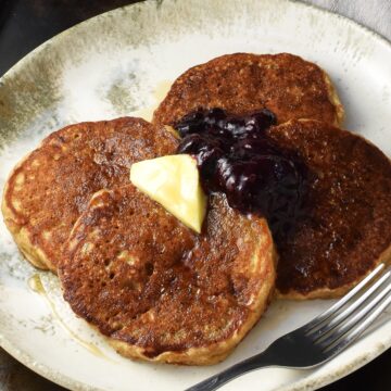 Side view of quinoa pancakes topped with butter and fruit mixture on white plate with fork.