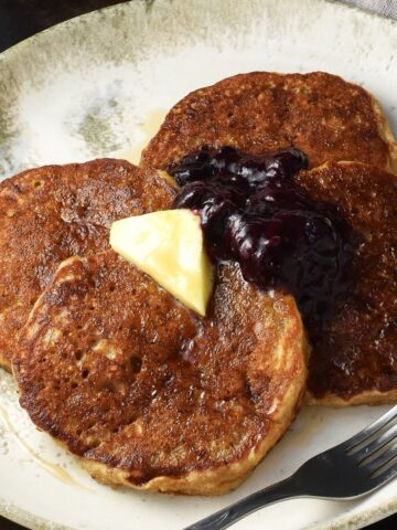 Side view of quinoa pancakes topped with butter and fruit mixture on white plate with fork.