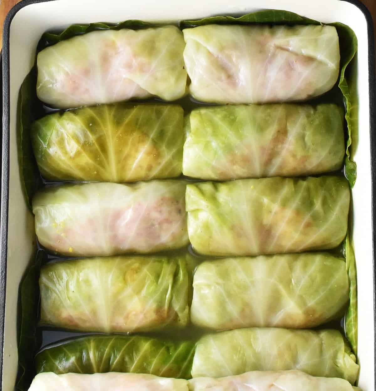 Uncooked Polish cabbage rolls with stock in rectangular dish.