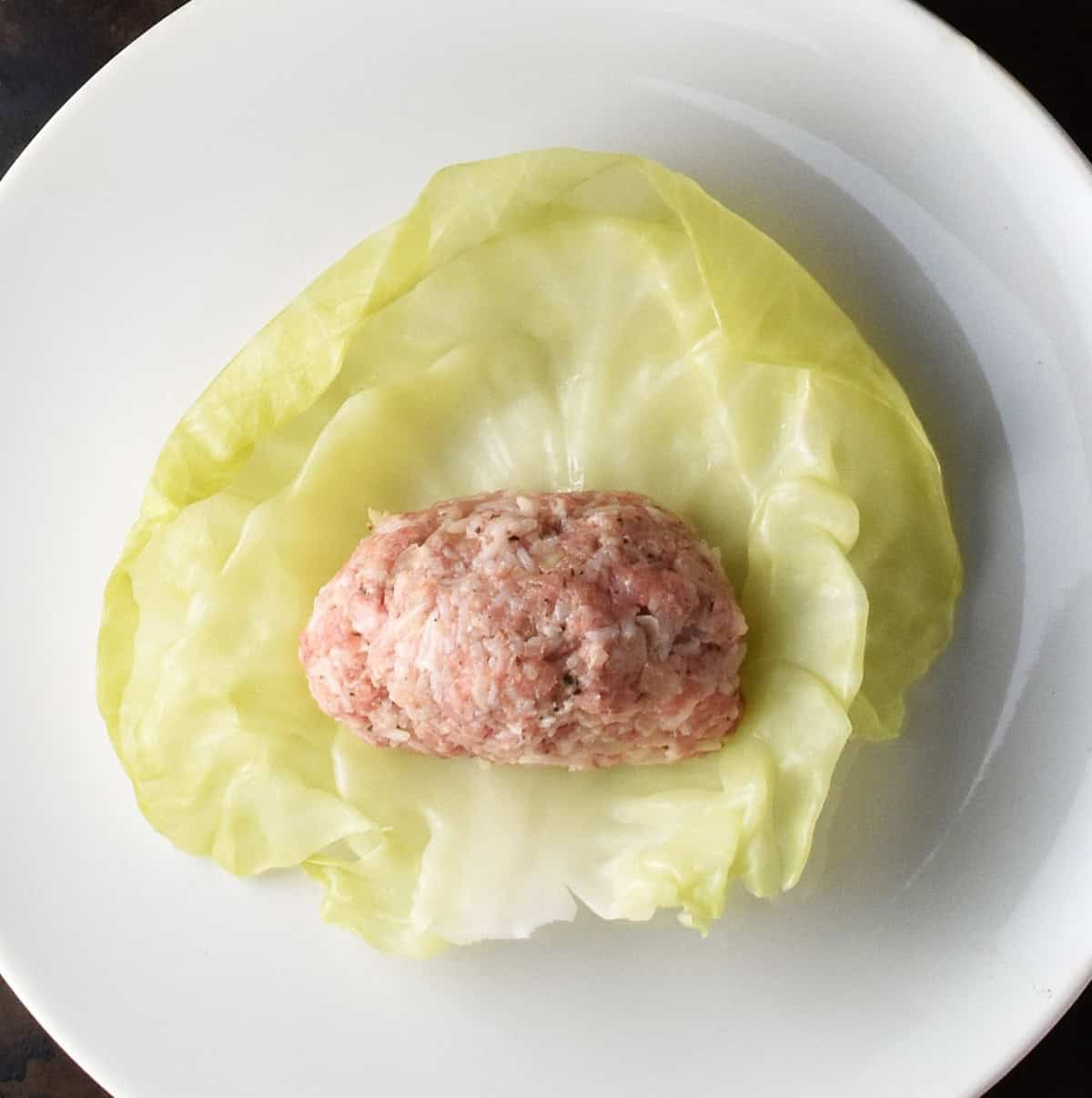 Cabbage leaf with golabki filling mixture on top of white plate.