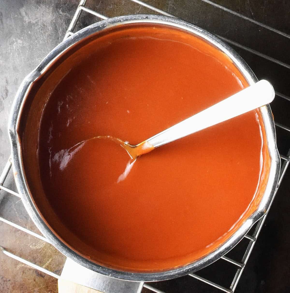 Top down view of smooth tomato sauce with spoon in metal saucepan.