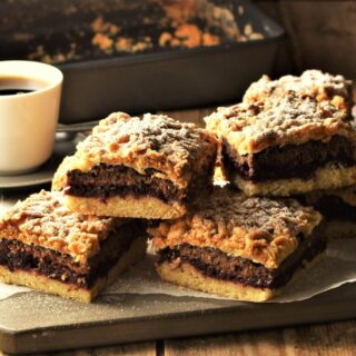 Side view of coffee cake slices on top of parchment with cup of coffee in background.