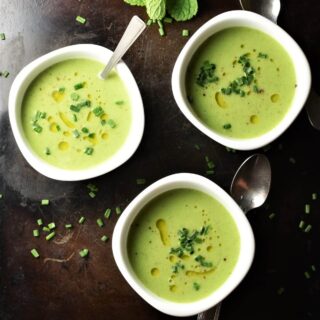 Top down view of creamy cold cucumber soup in 3 white bowls with spoons.