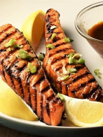 Close-up view of grilled marinated salmon with lemon wedges and hoisin sauce.