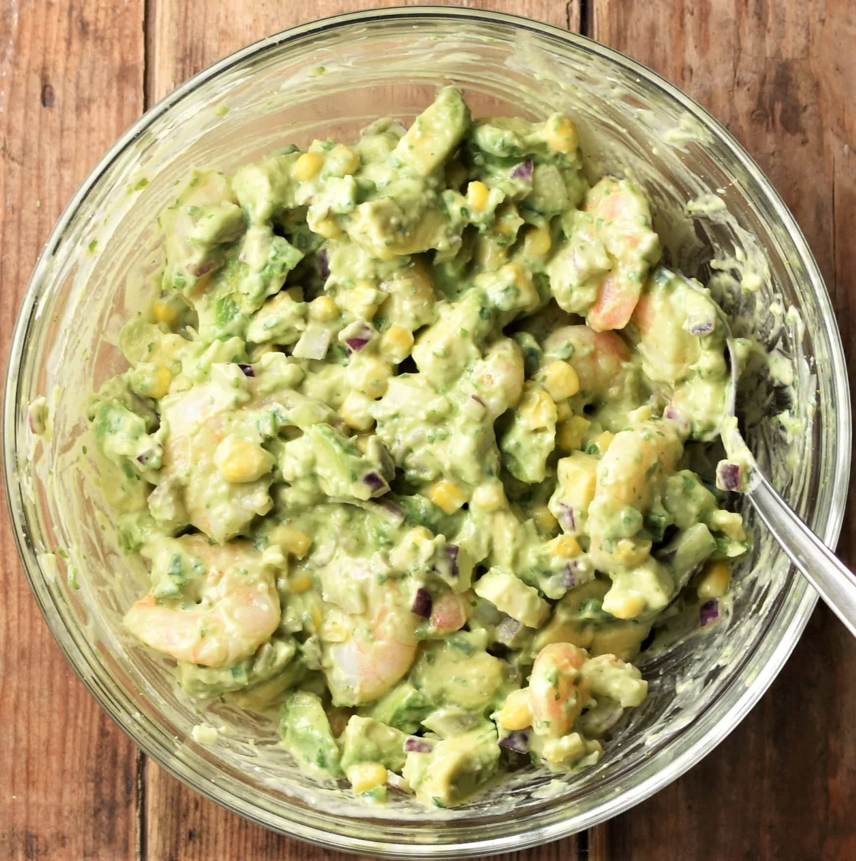 Creamy avocado and shrimp mixture in mixing bowl with spoon.