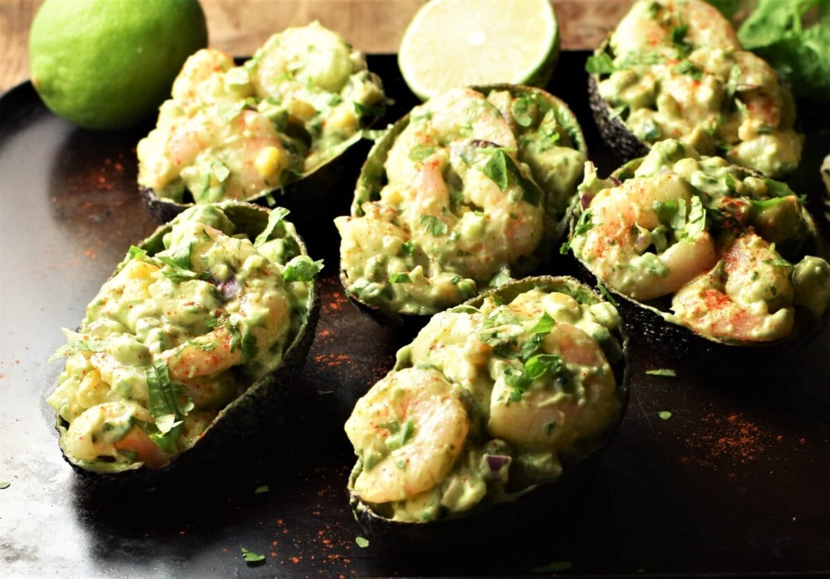 Shrimp stuffed avocado halves with limes in background.