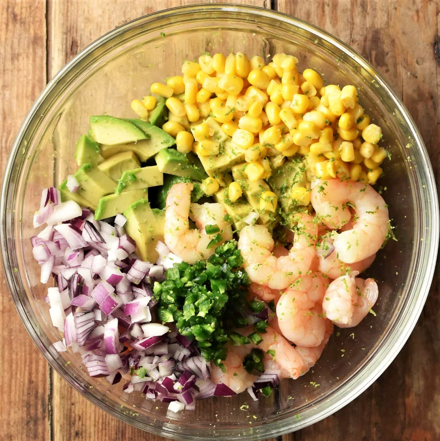 Shrimp, diced avocado, corn, chopped red onion and herbs in mixing bowl.