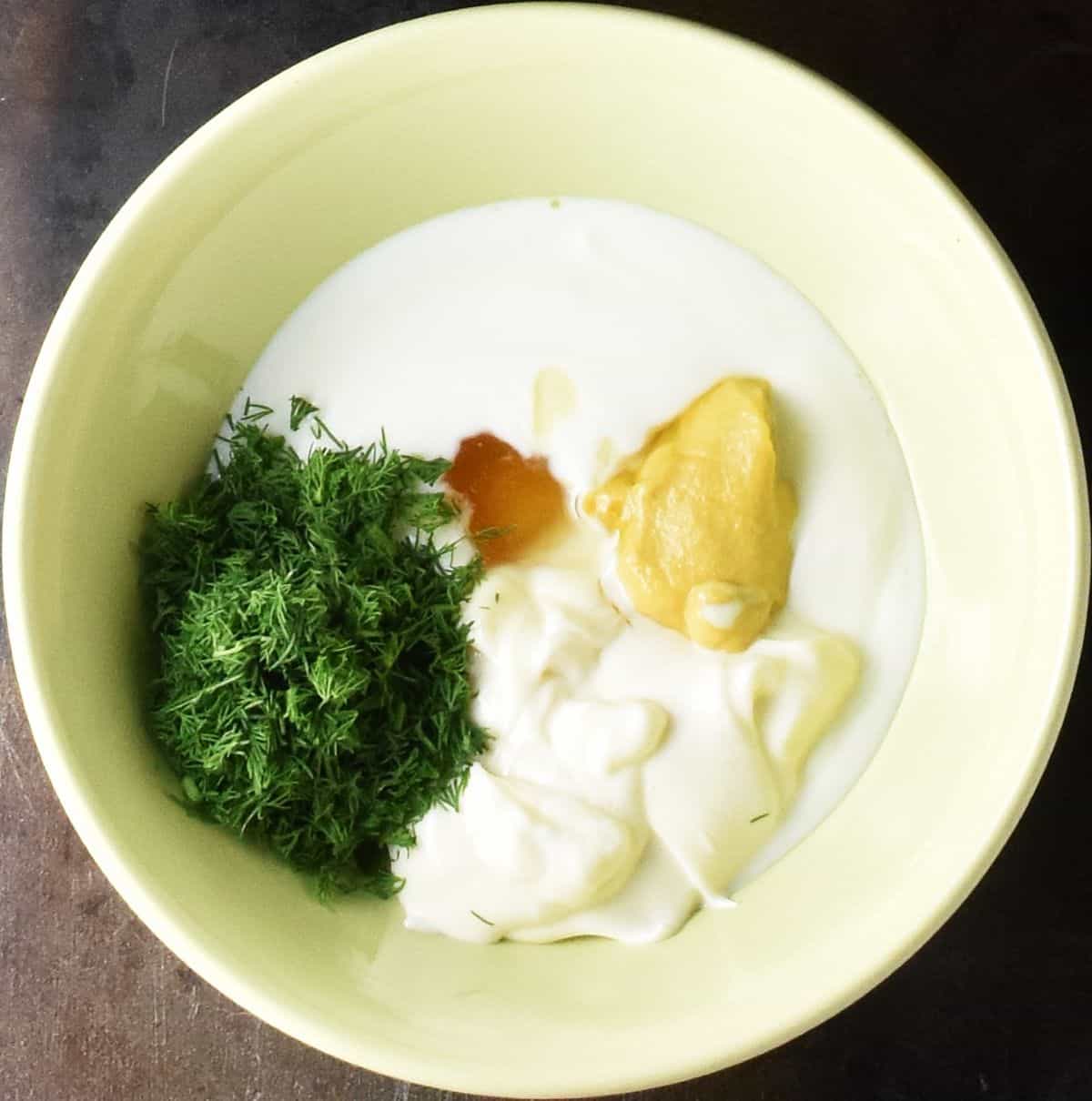 Yogurt, mustard and chopped fresh dill in yellow bowl.