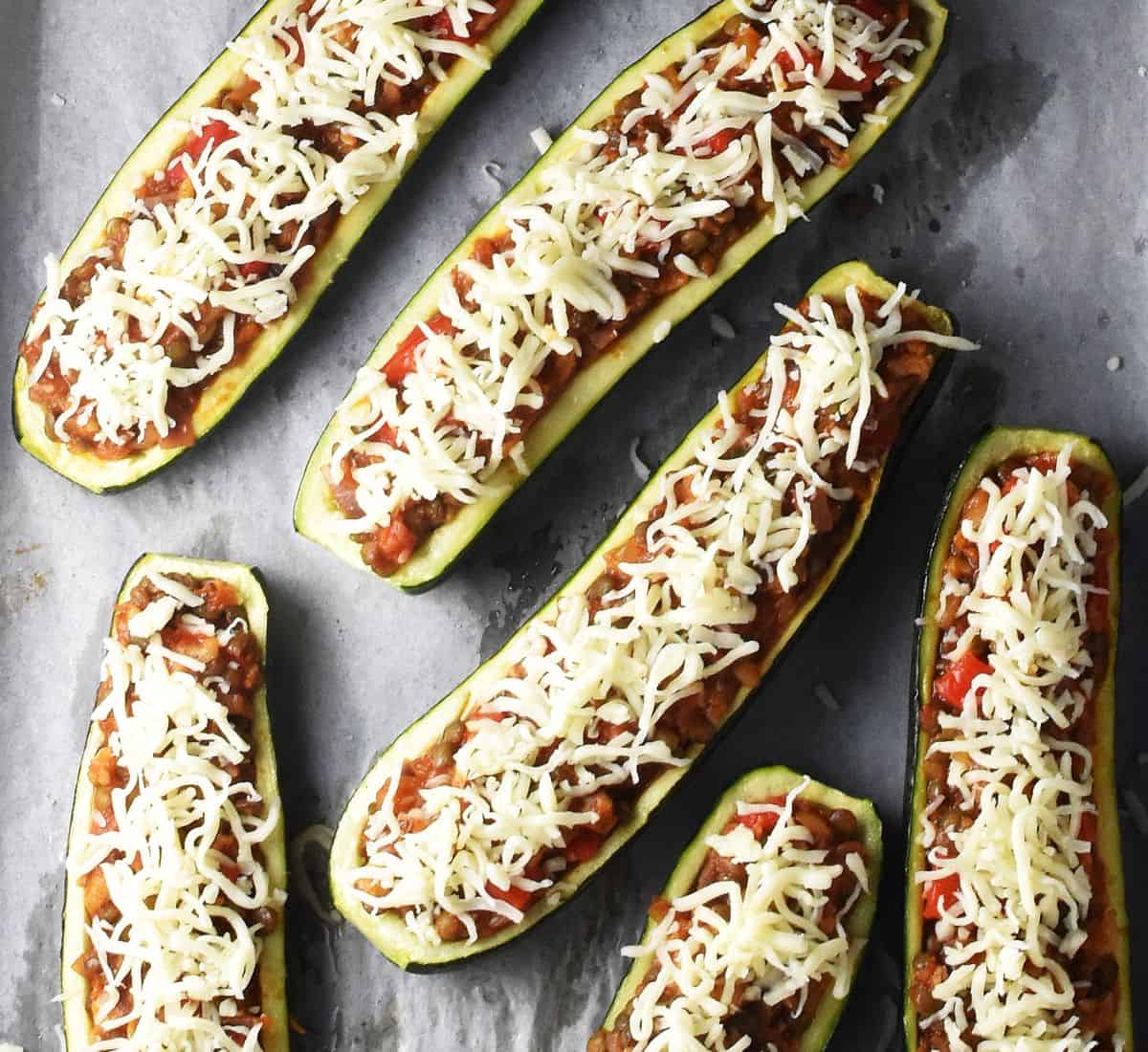 Top down view of zucchini boats topped with shredded cheese on parchment.