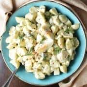Top down view of potato dill salad with eggs in blue bowl with spoon.