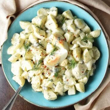 Top down view of potato dill salad with eggs in blue bowl with spoon.