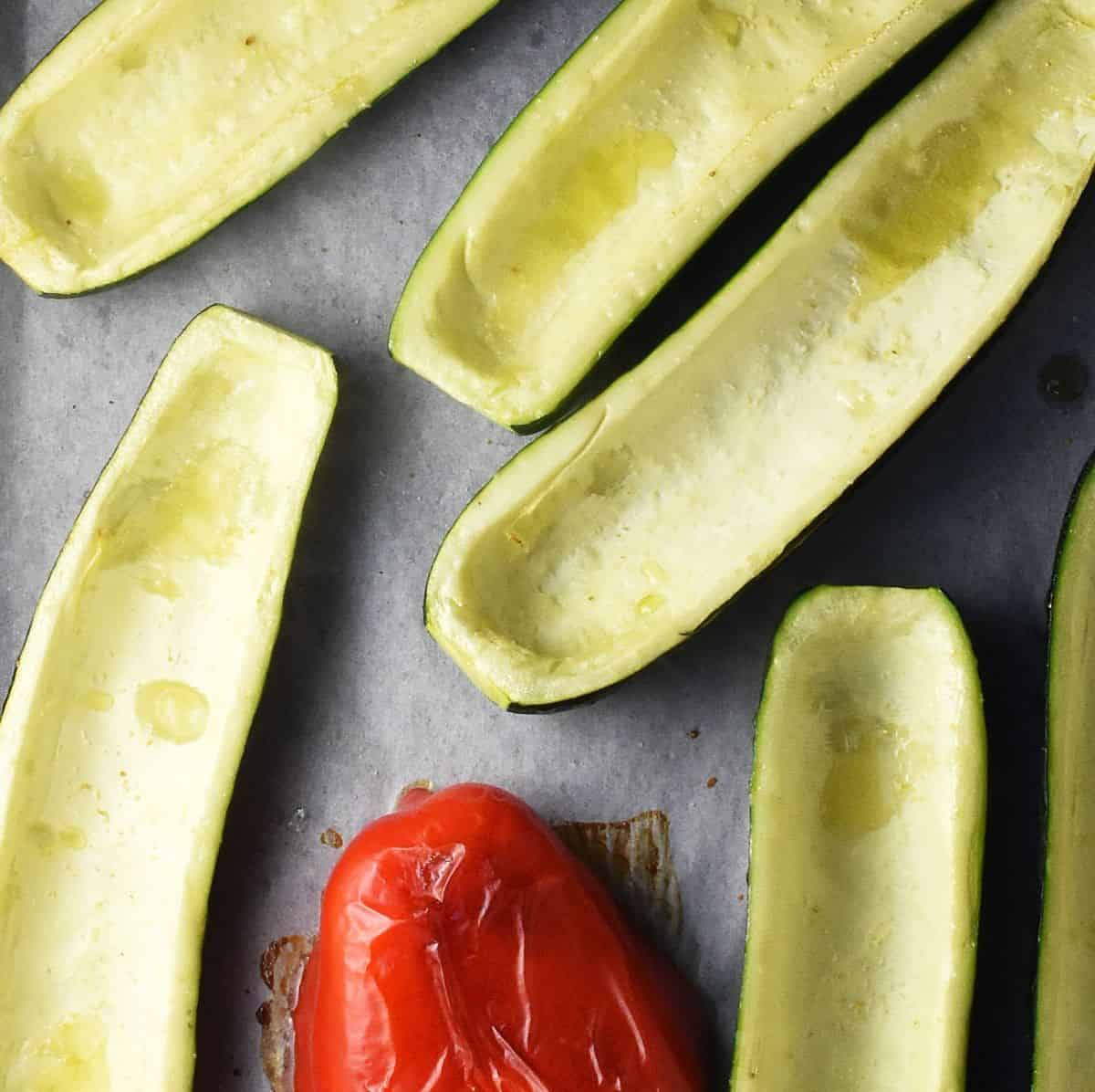 Hollowed out roasted zucchini boats and red pepper on parchment.