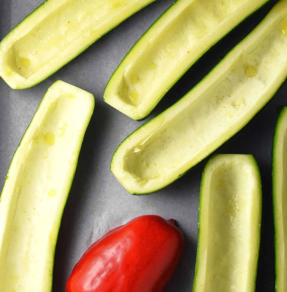 Raw zucchini boats and red pepper half on parchment.