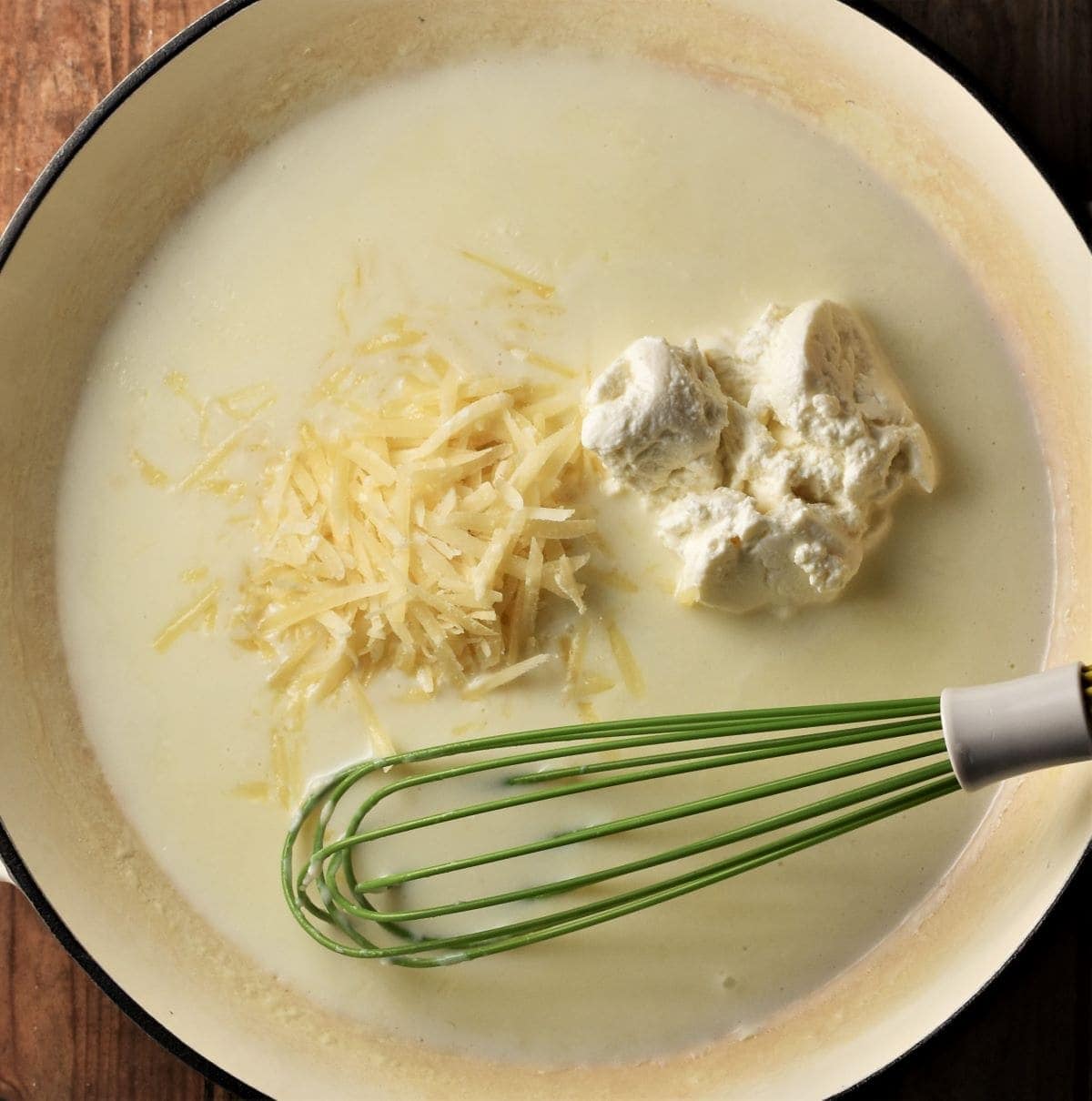 Creamy sauce with cheese in large white dish with green whisk.