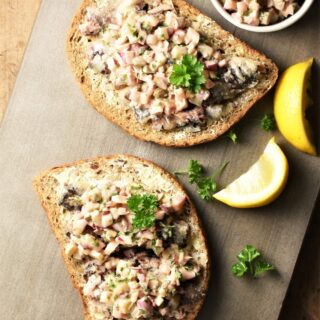 2 slices of toast with sardines and chopped vegetables on top, and lemon wedges in background.