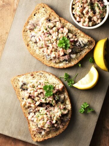 2 slices of toast with sardines and chopped vegetables on top, and lemon wedges in background.