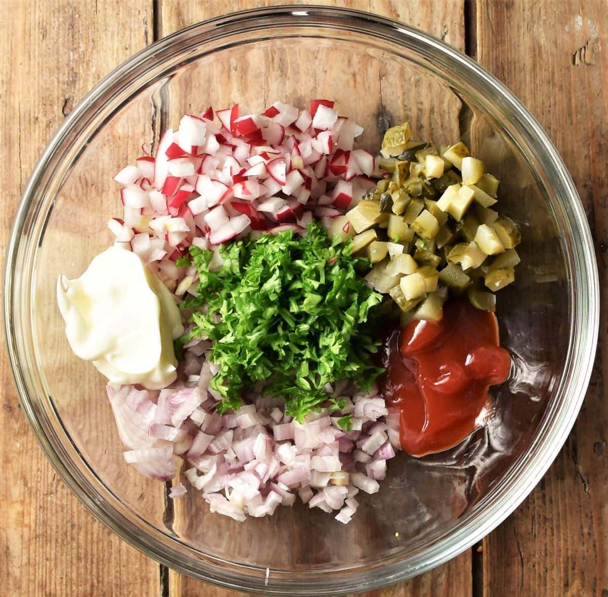 Chopped gherkins, shallots, radish, parsley and dollop of ketchup and mayonnaise in mixing bowl.