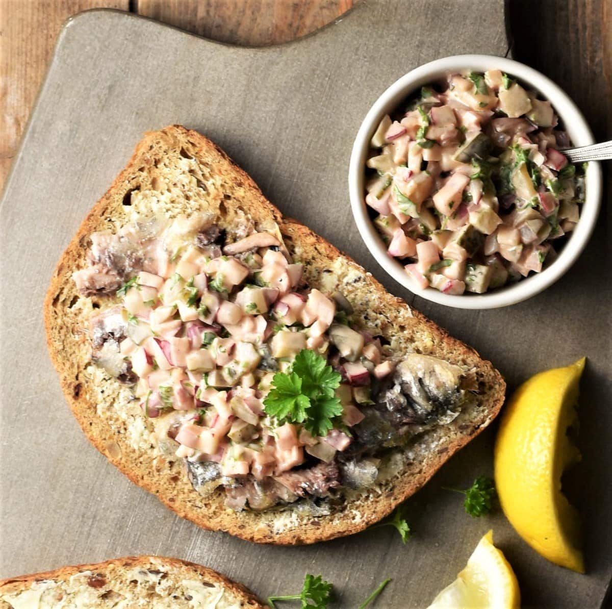 Toast with sardines and chunky topping mixture on top and in white dish.