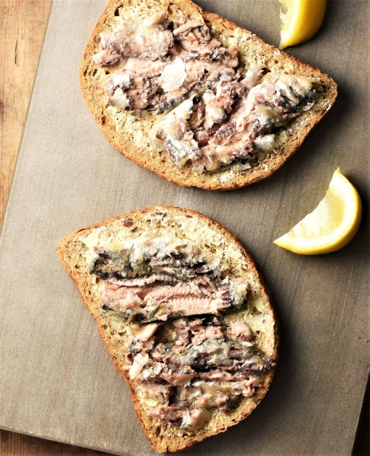 2 slices of bread with smashed sardines on top and lemon wedges in background.