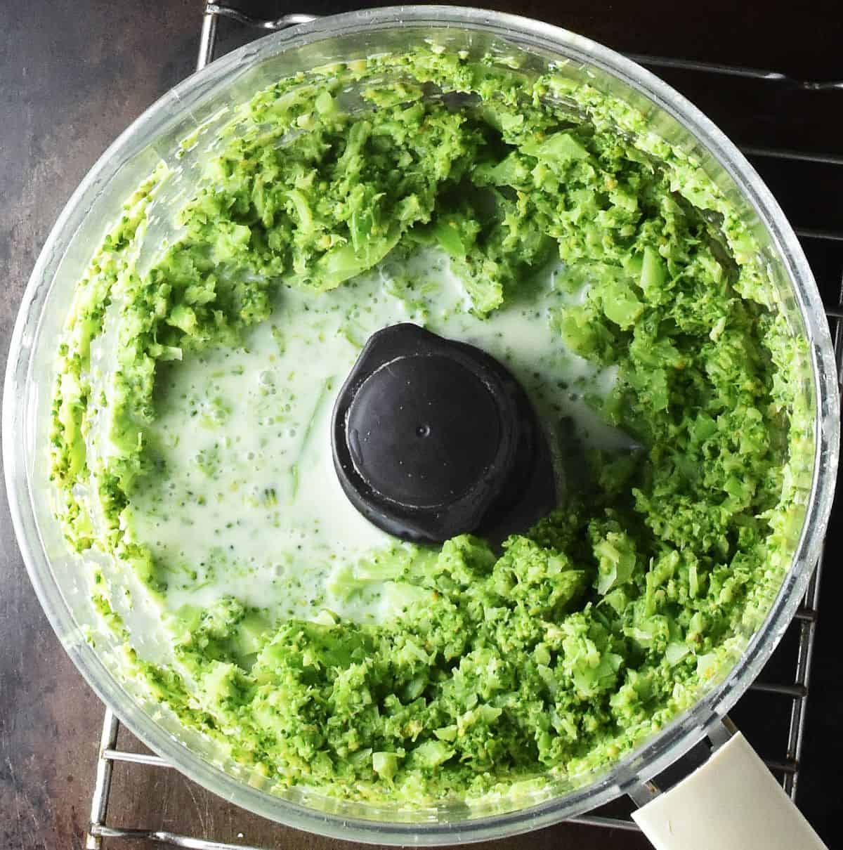 Top down view of chopped broccoli and milk in food processor bowl.