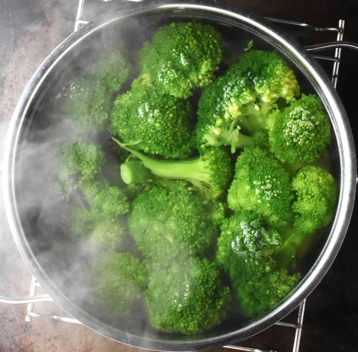 Broccoli florets in pot of water with steam visible.