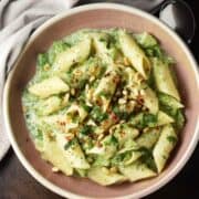 Top down view of creamy broccoli pasta with herbs in rustic pink bowl.
