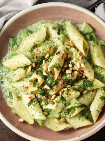 Top down view of creamy broccoli pasta with herbs in rustic pink bowl.