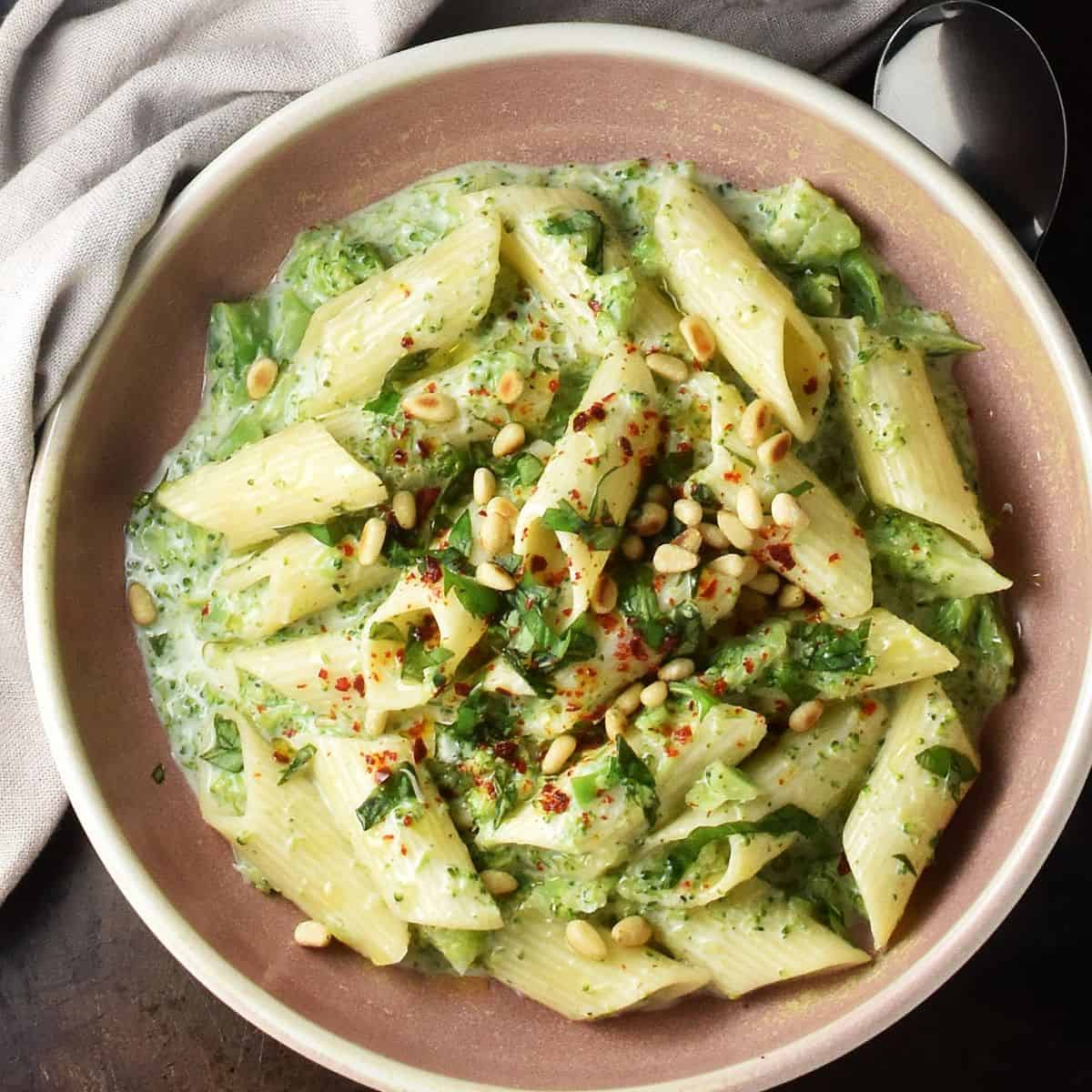Top down view of pasta with creamy broccoli sauce in rustic pink, shallow bowl.