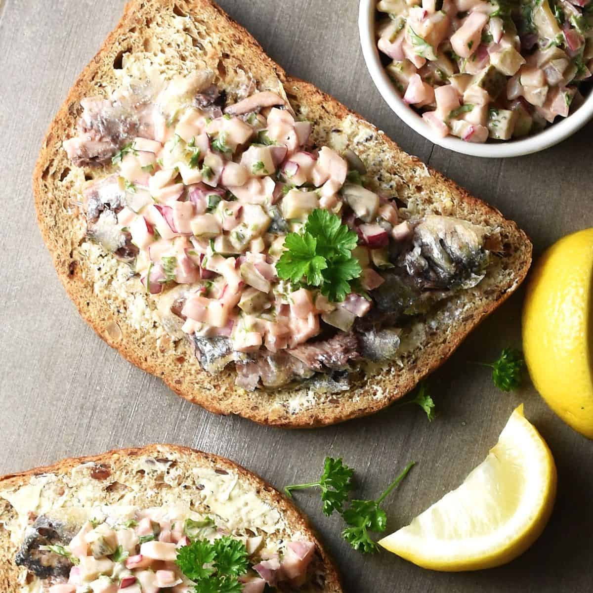 Top down view of sardines on toast with lemon wedges in background.