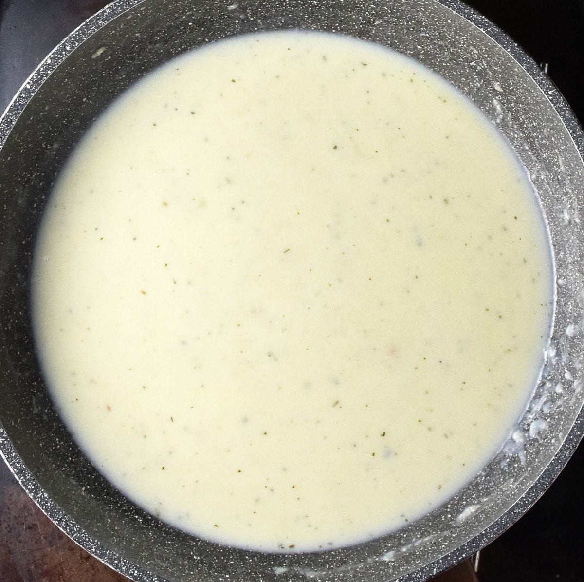 Top down view of white pasta sauce in large, grey pan.