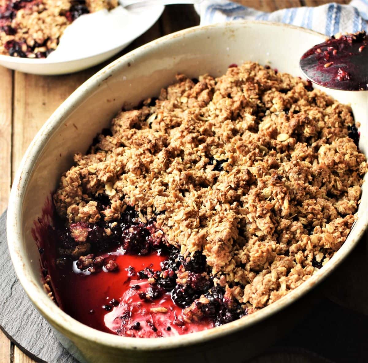 Side view of blackberry crumble in white oval dish.