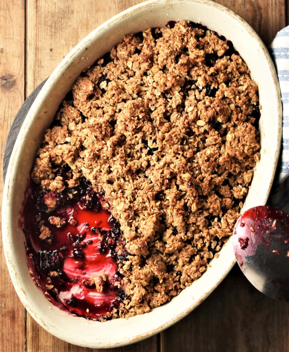 Top down view of blackberry crumble in white oval dish with spoon.