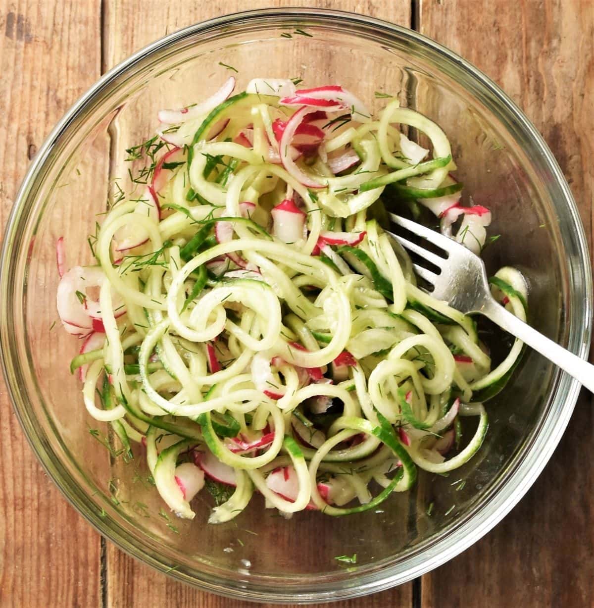 Cucumber and radish slaw in mixing bowl with fork.