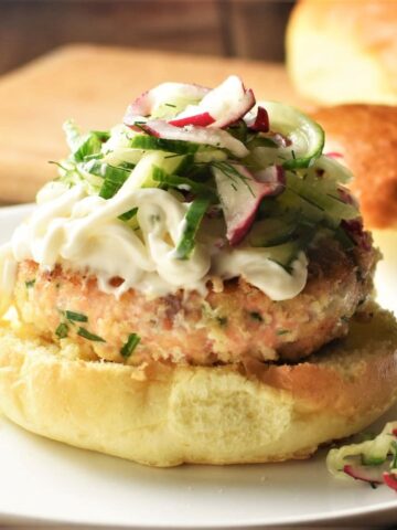 Salmon burger on top of bun with slaw and buns in background.