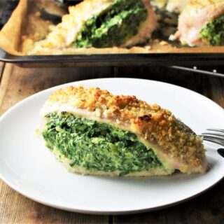 Side view of spinach and cheese stuffed chicken breast on top of plate with chicken in background.