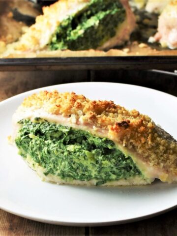 Side view of spinach and cheese stuffed chicken breast on top of plate with chicken in background.