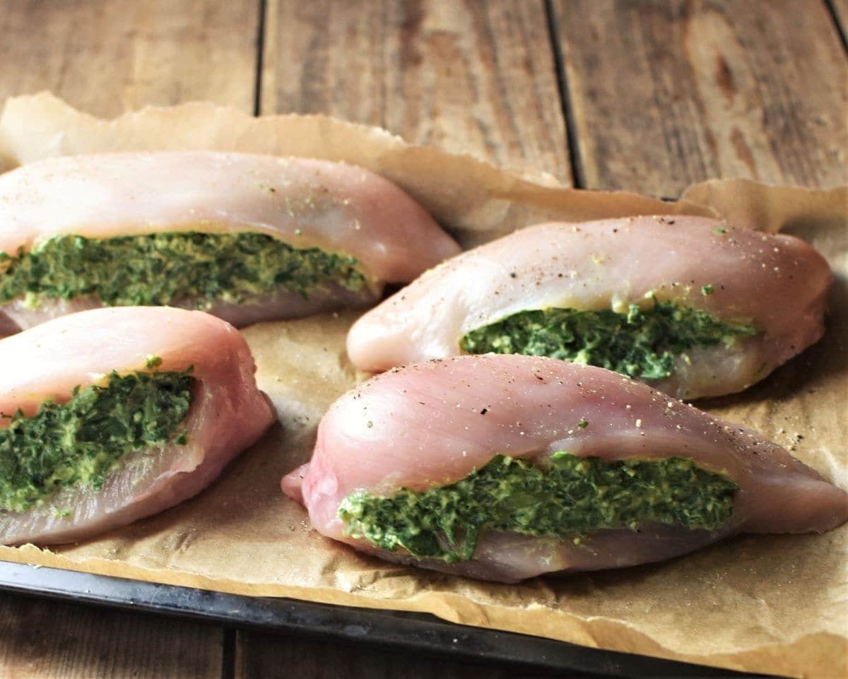 Side view of skinless raw chicken breasts stuffed with spinach on top of parchment.