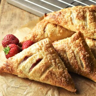 Side view of strawberry turnovers on top of parchment with fresh strawberries in background.